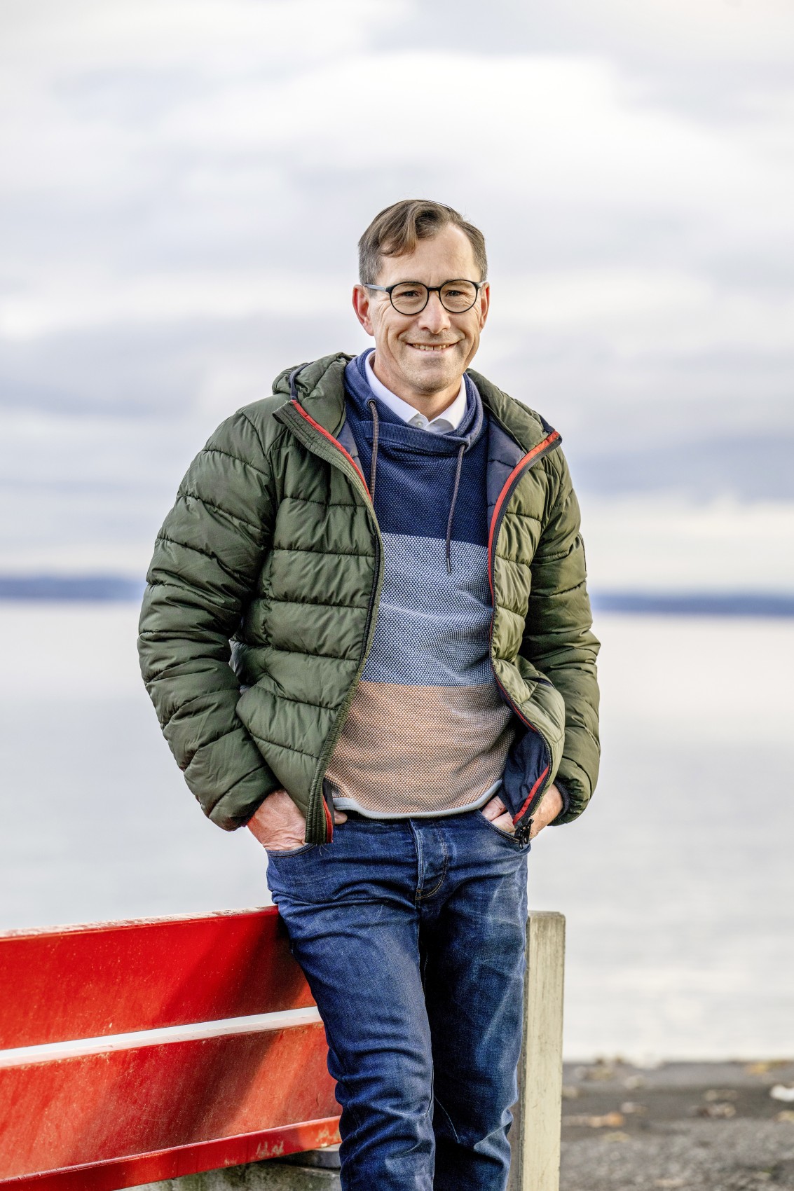 Arbons Stadtpräsident René Walther lehnt sich an eine rote Bank am Bodenseeufer.